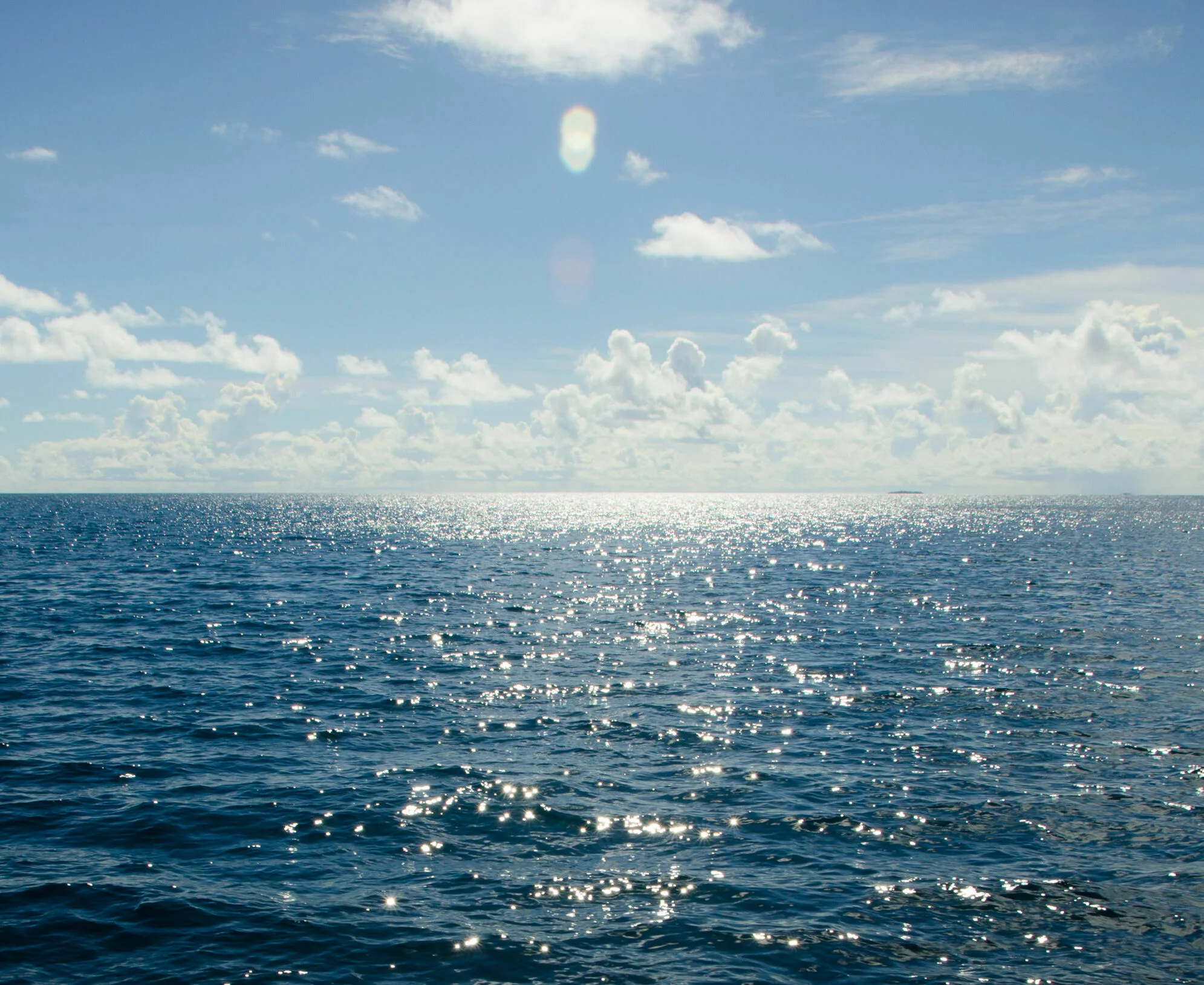 Weites Meer mit spiegelnder Wasserfläche, Himmel mit Wolken, Sonnenlicht spiegelt sich auf der Wasseroberfläche.
