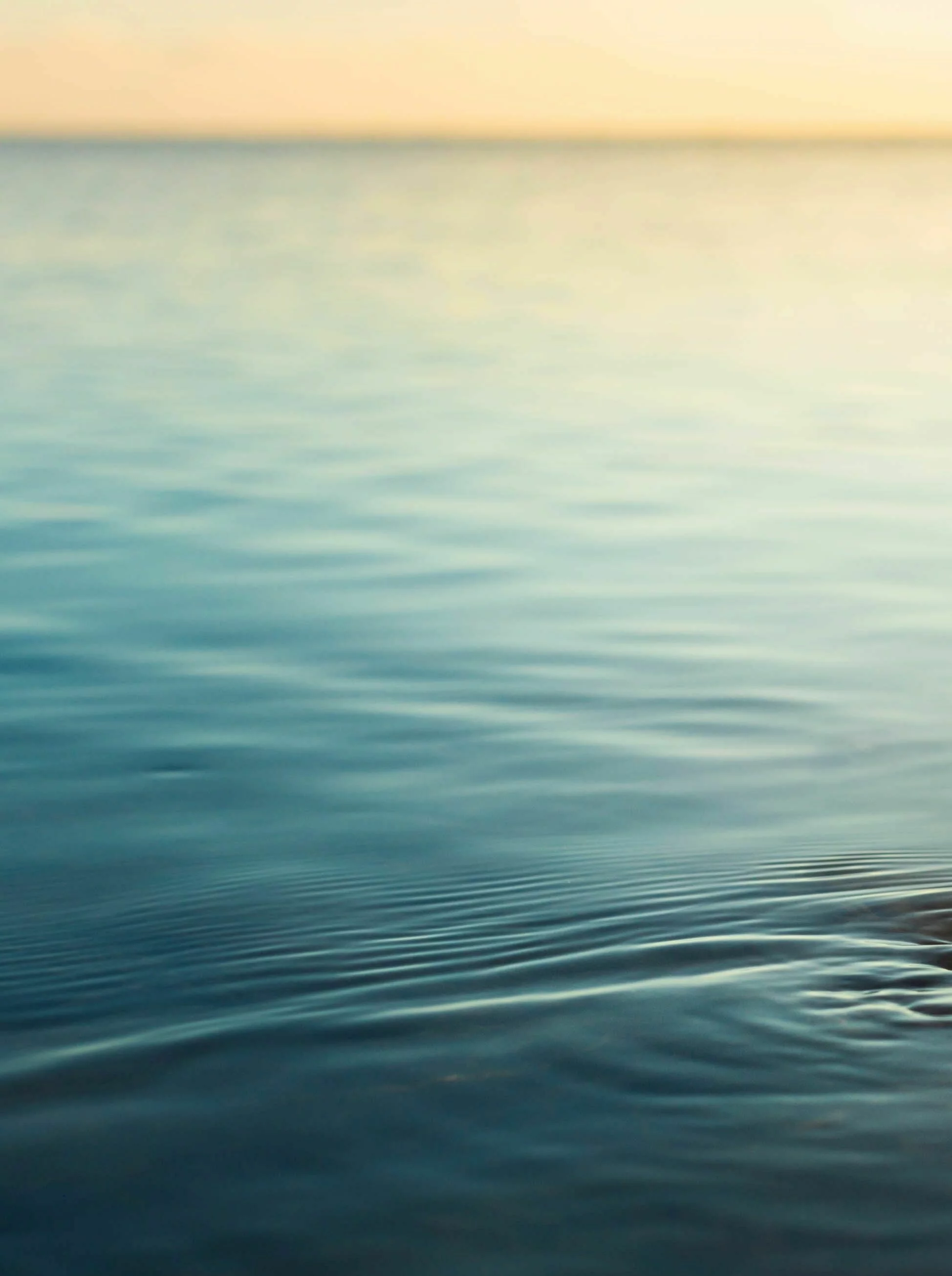 Menschenhand taucht in ruhiges Meerwasser bei Sonnenuntergang.